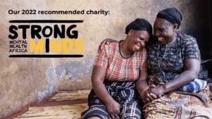 Two women sitting together, smiling, in a community setting in Africa.
