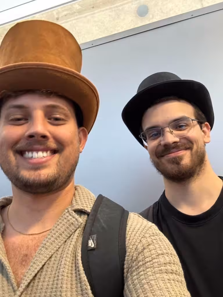 Two researchers from the Happier Lives Institute wearing top hats at the airport on their way to ISOLS 2025.
