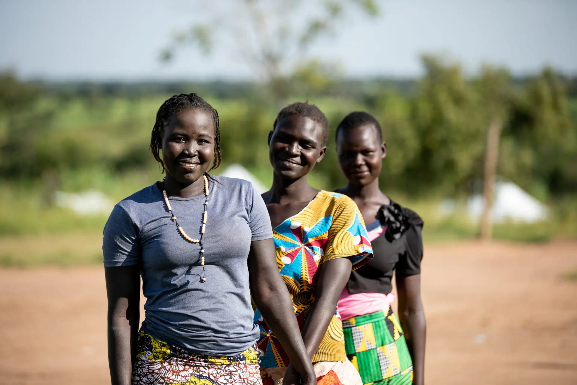 Women smiling outdoors in a rural setting.