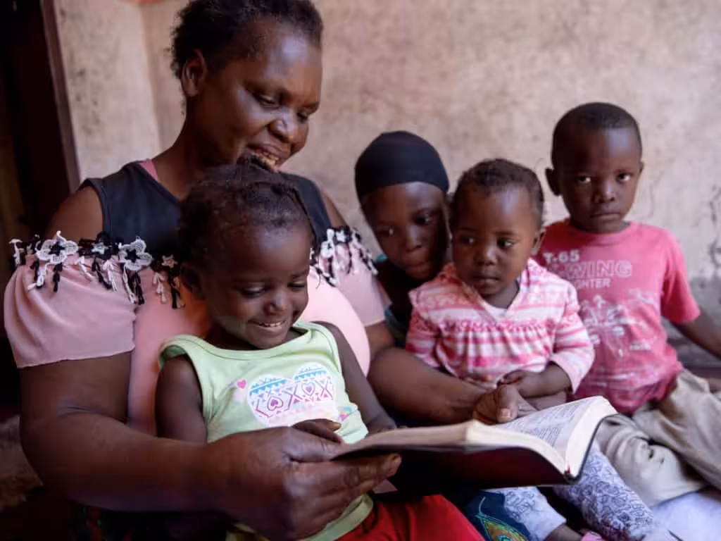 A woman reading a book to four children.