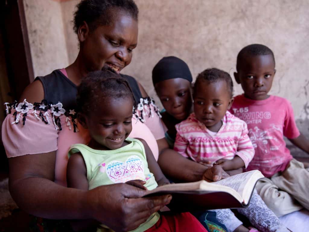 A woman reading a book to four children.