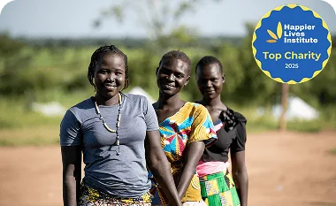 Smiling women in colorful traditional clothing outdoors in a rural setting.