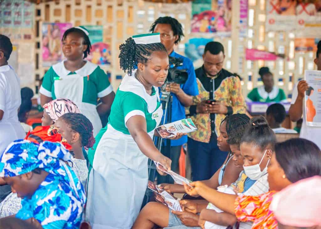 Healthcare workers distributing informational materials to a group of mothers attending a health outreach event in Ghana.