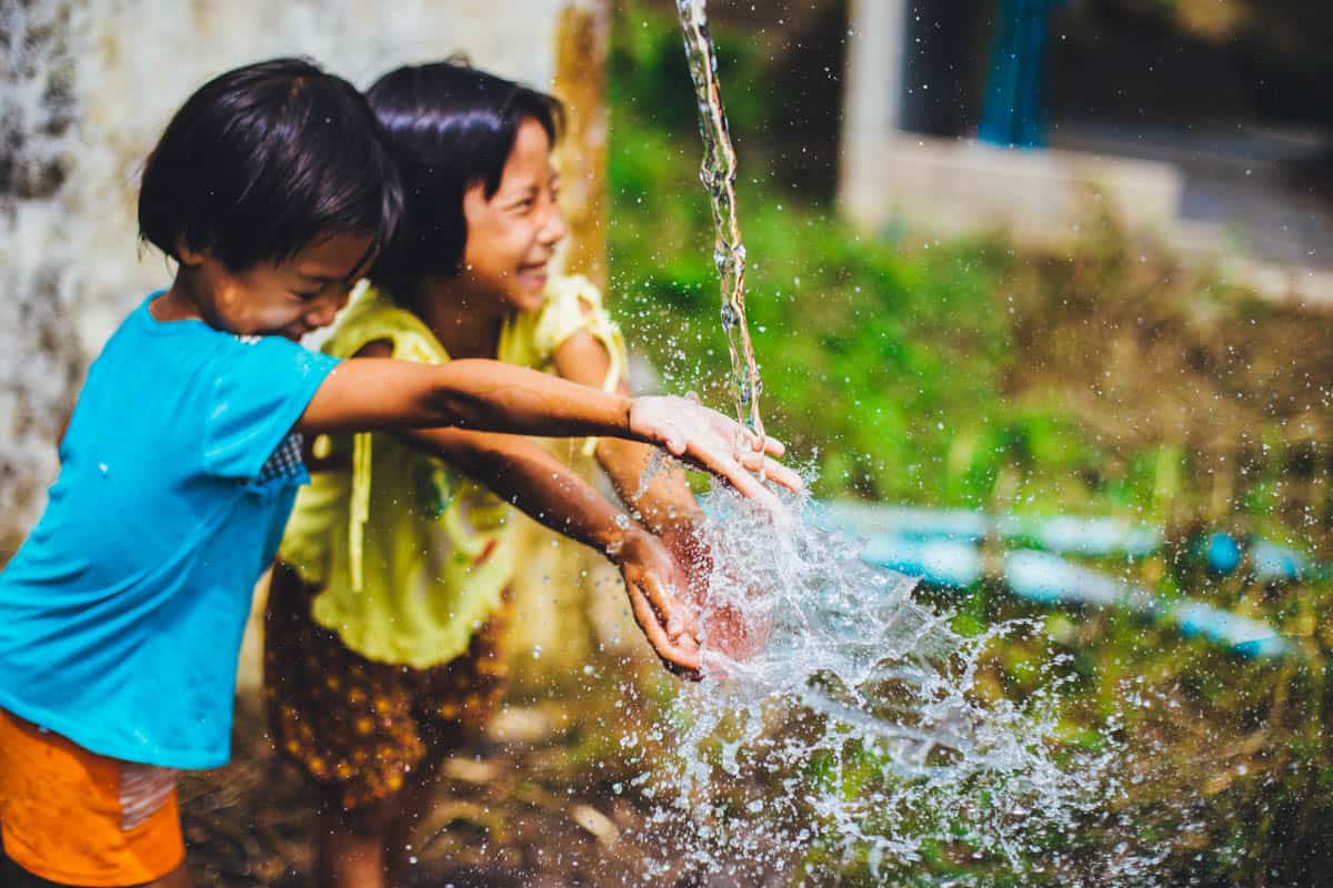 Children playing with water outdoors, smiling and enjoying nature.