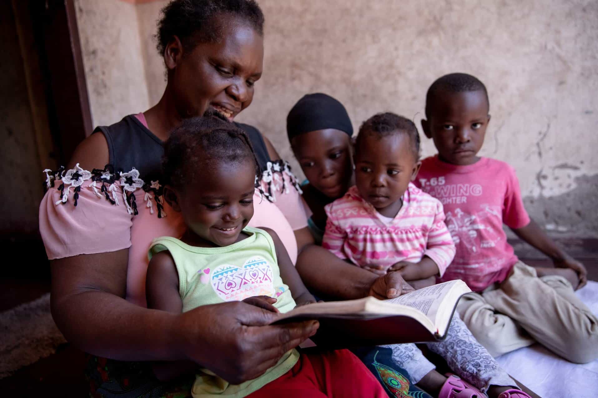 A woman reading a book to four children.