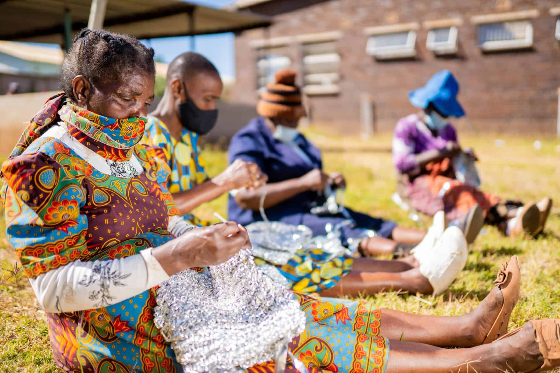 Women in traditional attire sitting outdoors, engaging in a craft activity on a
sunny day.