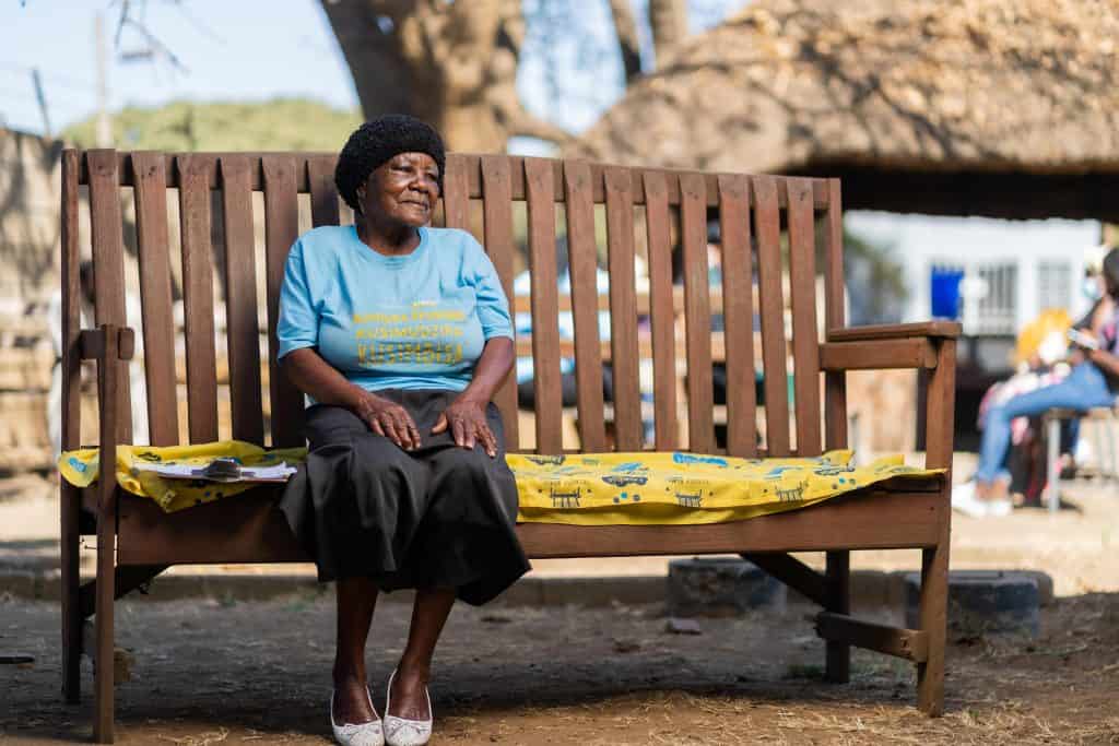An elderly woman sitting thoughtfully on a Friendship Bench in Zimbabwe.
