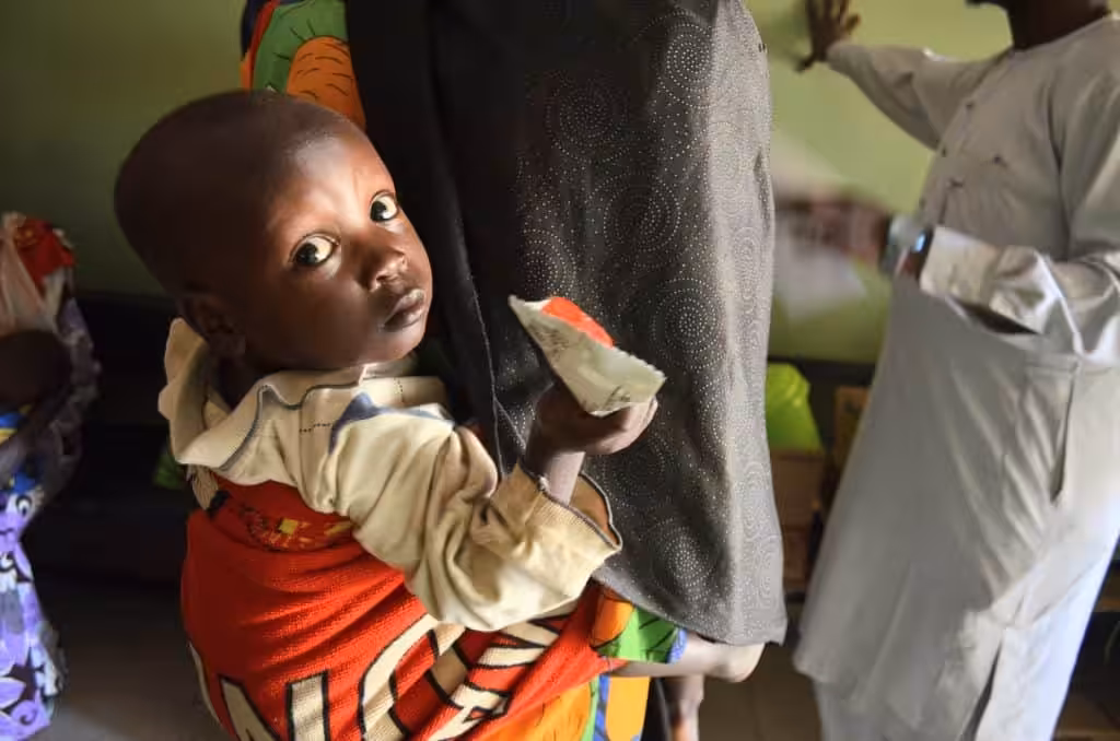 A child receiving aid in a community setting, looking at the camera with curiosity.