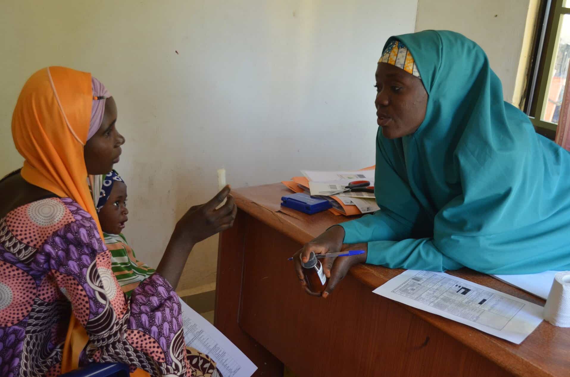 A woman holding her young child in her arms while she consults with a healthcare
worker about malnutrition in a community health setting.