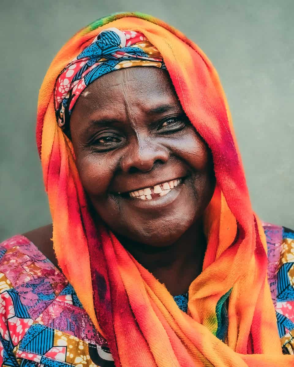 Smiling woman wearing colorful traditional dress and vibrant headwrap, radiating warmth and happiness.