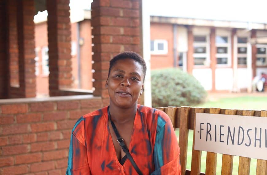 A woman in colorful attire sitting near a “Friendship” sign, representing community and social connection.