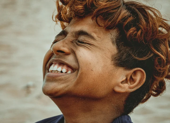 Young man smiling with eyes closed, enjoying a joyful moment outside.