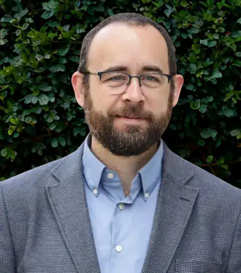 Portrait of a man with glasses and beard in a suit.