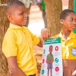 Two children in Ghana holding a sign that explains the effects of lead on the child.