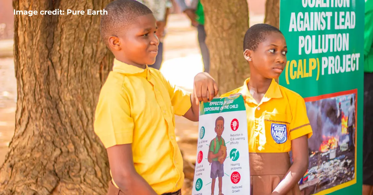 Two children in Ghana holding a sign that explains the effects of lead on the child.