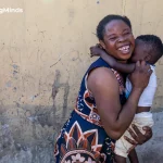Smiling woman holding a child against a yellow wall in Africa.