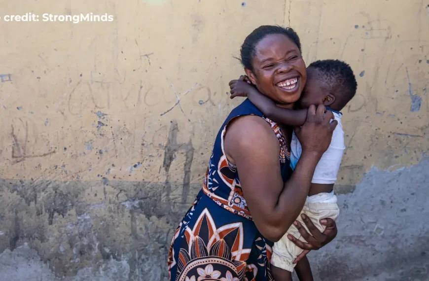 Smiling woman holding a child against a yellow wall in Africa.