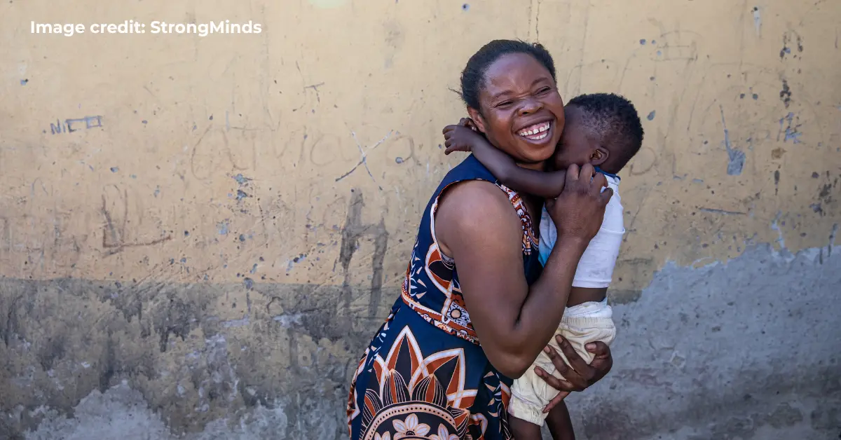 Smiling woman holding a child against a yellow wall in Africa.