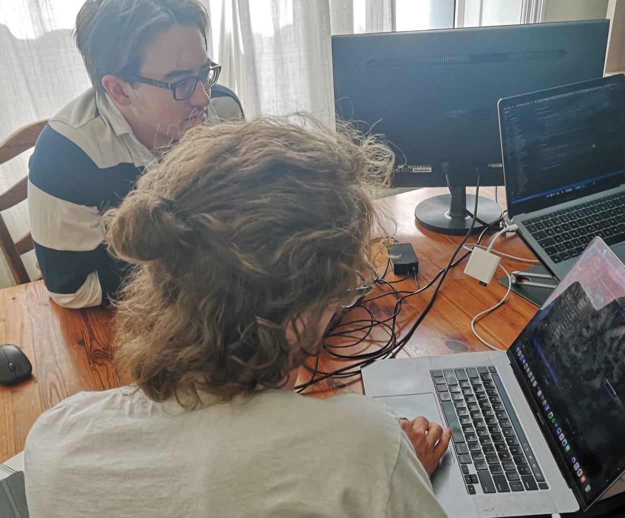 Two researchers sharing a table, one looking across at the other's screen as they work through an analysis.