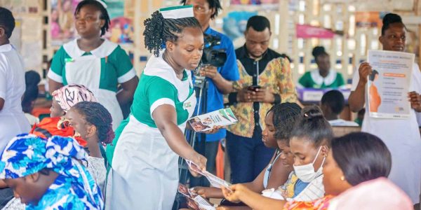 Healthcare workers distributing informational materials to a group of mothers attending a health outreach event in Ghana.