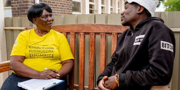 A talk therapy session between a man and a peer counsellor on a Friendship Bench.